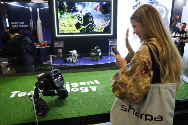 An attendee waves at the Sentigent Technology ROVAR X3 outdoor companion robot as it is demonstrated during the annual Consumer Electronics Show (CES) in Las Vegas, Nevada on January 7, 2026. (Photo by Patrick T. Fallon / AFP)