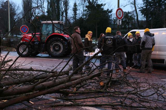 Farmers gather next to tree trunks placed across a road to block a road at Porte d'Auteuil during a demonstration of French farmers union FDSEA as part of a nationwide day of protests and actions called by several farmers unions to push French government to block the Mercosur trade deal and protest against its handling of the nodular dermatitis (CND) epidemic, in Paris on January 8, 2026. (Photo by Thomas SAMSON / AFP)