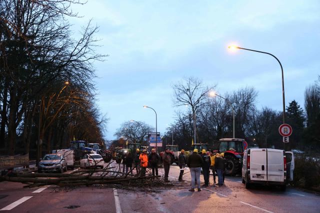 Farmers gather next to tree trunks placed across a road to block a road at Porte d'Auteuil during a demonstration of French farmers union FDSEA as part of a nationwide day of protests and actions called by several farmers unions to push French government to block the Mercosur trade deal and protest against its handling of the nodular dermatitis (CND) epidemic, in Paris on January 8, 2026. (Photo by Thomas SAMSON / AFP)