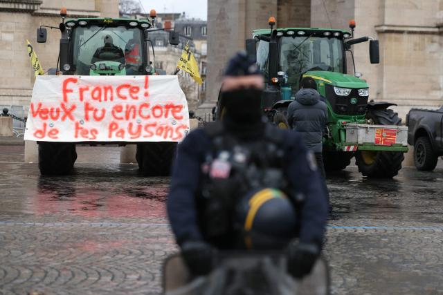 A French Republicain Security Corps (CRS) police officer stands next tractors, including one with a banner reading "France! Do you still want your farmers?", parked in front of the Arc de Triomphe during a demonstration of French agricultural union Coordination Rurale (CR) as part of a nationwide day of protests and actions called by several farmers unions to push the French government to block the Mercosur trade deal and protest against its handling of the nodular dermatitis (CND) epidemic, in Paris on January 8, 2026. (Photo by Thomas SAMSON / AFP)
