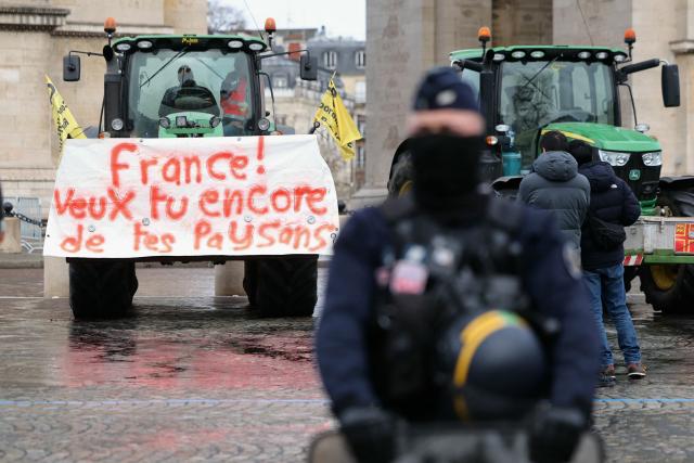 A French Republicain Security Corps (CRS) police officer stands next tractors, including one with a banner reading "France! Do you still want your farmers?", parked in front of the Arc de Triomphe during a demonstration of French agricultural union Coordination Rurale (CR) as part of a nationwide day of protests and actions called by several farmers unions to push the French government to block the Mercosur trade deal and protest against its handling of the nodular dermatitis (CND) epidemic, in Paris on January 8, 2026. (Photo by Thomas SAMSON / AFP)