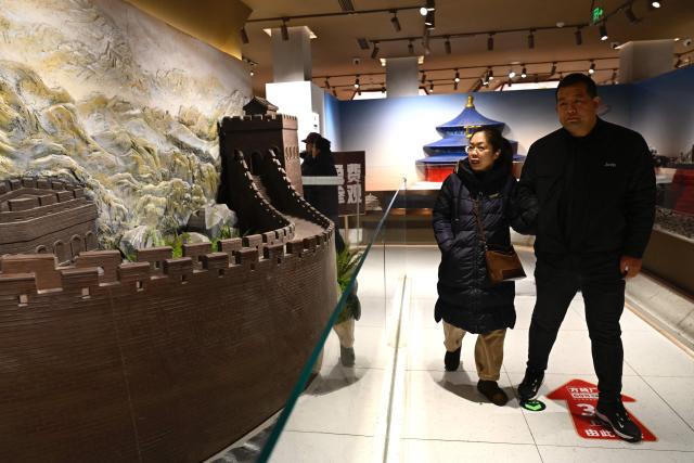 A couple walks past a model of the Great Wall of China made from chocolate at a chocolate shop in Beijing on January 8, 2026. (Photo by WANG Zhao / AFP)
