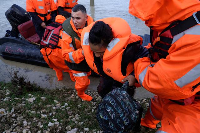 A woman is evacuated by members of the Civil Emergencies near the Vjosa River in the village of Novosele, near Vlore on January 8, 2026. Heavy rainfall in recent days has caused major flooding in cities, rivers overflowing their banks, and blockages on national roads across Albania. (Photo by Adnan Beci / AFP)