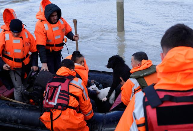 A woman sits with her dogs on a lifeboat during their evacuation by members of the Civil Emergencies near the Vjosa River in the village of Novosele, near Vlore on January 8, 2026. Heavy rainfall in recent days has caused major flooding in cities, rivers overflowing their banks, and blockages on national roads across Albania. (Photo by Adnan Beci / AFP)