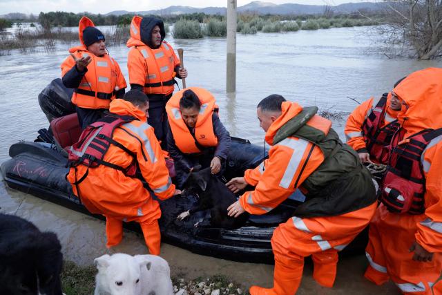 A woman sits with her dogs on a lifeboat during their evacuation by members of the Civil Emergencies near the Vjosa River in the village of Novosele, near Vlore on January 8, 2026. Heavy rainfall in recent days has caused major flooding in cities, rivers overflowing their banks, and blockages on national roads across Albania. (Photo by Adnan Beci / AFP)