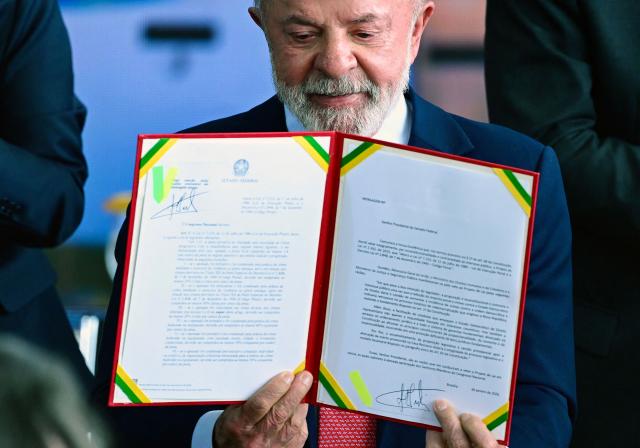 Brazil’s President Luiz Inacio Lula da Silva shows the veto on the law reducing sentences for those convicted of attempted coup during the Ceremony in Defense of Democracy marking the third anniversary of the attempted coup d'йtat involving the invasion and destruction of buildings of the three branches of government, at the Planalto Palace in Brasнlia, on January 8, 2026. (Photo by Evaristo Sa / AFP)