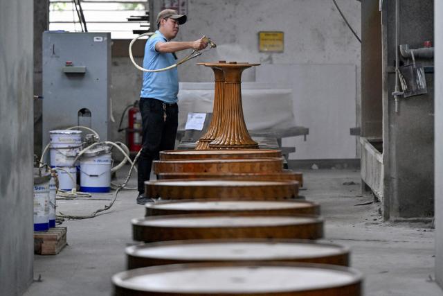 This photo taken on November 4, 2025 shows an employee working inside the Jonathan Charles Fine Furniture factory in Ho Chi Minh City. Over the whine of buzzsaws and the steady whir of sanders, hundreds of Vietnamese workers in a factory outside Ho Chi Minh City hustle to fill orders for high-end furniture. It will adorn luxury hotels and residences across the Middle East, Europe and the United States, where the Vietnam-based Jonathan Charles furniture company has largely shrugged off US President Donald Trump's tariffs. (Photo by Nhac NGUYEN / AFP)