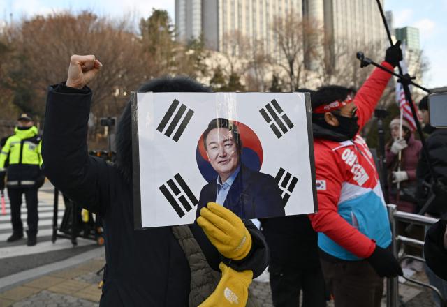 A supporter of South Korea's former impeached president Yoon Suk Yeol holds a placard showing a picture of Yoon in front of the Seoul Central District Court in Seoul on January 9, 2026, as Yoon's final criminal trial on insurrection charges is held in the court. (Photo by Jung Yeon-je / AFP)