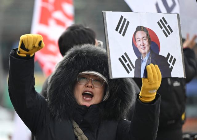 A supporter of South Korea's former impeached president Yoon Suk Yeol holds up a placard showing a picture of Yoon in front of the Seoul Central District Court in Seoul on January 9, 2026, as Yoon's final criminal trial on insurrection charges is held in the court. (Photo by Jung Yeon-je / AFP)