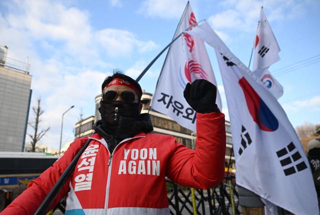 A supporter of South Korea's former impeached president Yoon Suk Yeol carries a large national flag in front of the Seoul Central District Court in Seoul on January 9, 2026, as Yoon's final criminal trial on insurrection charges is held in the court. (Photo by Jung Yeon-je / AFP)