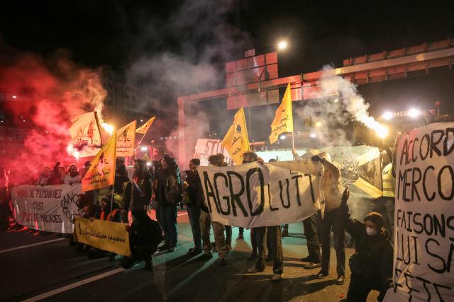 Members of the Confederation Paysanne farmers union hold up banners during an action aimed at slowing down the traffic with tractors on Paris' ring road by Porte de Montreuil, to push the French government to block the Mercosur trade deal and protest against its handling of the nodular dermatitis (CND) epidemic, in Paris on January 9, 2026. (Photo by Thomas SAMSON / AFP)