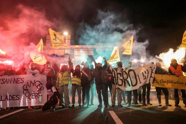 TOPSHOT - Members of the Confederation Paysanne farmers union hold up banners during an action aimed at slowing down the traffic with tractors on Paris' ring road by Porte de Montreuil, to push the French government to block the Mercosur trade deal and protest against its handling of the nodular dermatitis (CND) epidemic, in Paris on January 9, 2026. (Photo by Thomas SAMSON / AFP)