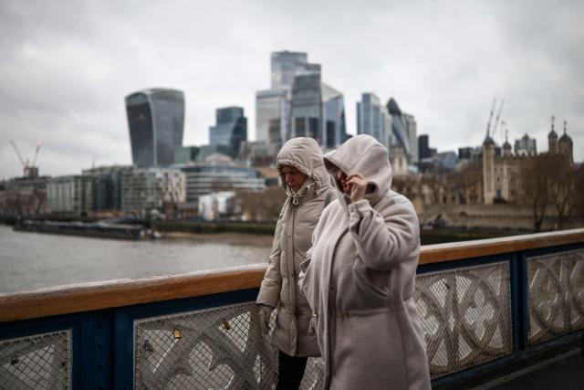Pedestrians, wrapped up in winter clothing, walk across the River Thames on a cold, grey day in central London on January 9, 2026. The United Kingdom, France and Germany shivered through severe winter weather on January 9, with tens of thousands of homes suffering the cold snap without power. (Photo by Henry NICHOLLS / AFP)