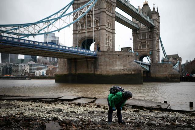 A person mudlarks along the River Thames next to Tower Bridge (behind) on a cold, grey day in central London on January 9, 2026. The United Kingdom, France and Germany shivered through severe winter weather on January 9, with tens of thousands of homes suffering the cold snap without power. (Photo by Henry NICHOLLS / AFP)
