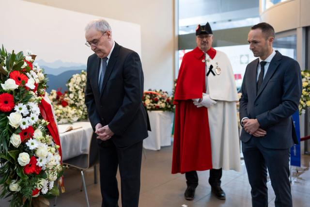 Switzerland's President Guy Parmelin (L) and State Councillor and President of the Council of State of the Canton of Valais, Mathias Reynard (R) stand before a floral wreath ahead of a tribute ceremony for the victims of the deadly fire that ripped through the bar Le Constellation in Crans-Montana on New Year's Eve, in Martigny on January 9, 2026. All of Switzerland will mark a national day of mourning on January 9 for the dozens of mostly teenagers killed when fire ravaged a ski resort bar crammed with New Year revellers. Just over a week after the tragedy at the Le Constellation bar in Crans-Montana, which left 40 dead and 116 injured, the wealthy Alpine nation will come to a standstill for a minute of silence at 2:00 pm (1300 GMT). (Photo by MICHAEL BUHOLZER / POOL / AFP)