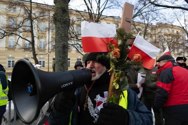 A participant shouts into a megaphone as he holds a crucifix decorated with Polish national flags, during a protest against the EU-Mercosur agreement in Warsaw, Poland on January 9, 2026. The EU gave on January 9, 2025 a long-delayed go, ahead to a huge trade deal with South American bloc Mercosur championed by business groups but loathed by many European farmers. (Photo by Wojtek RADWANSKI / AFP)