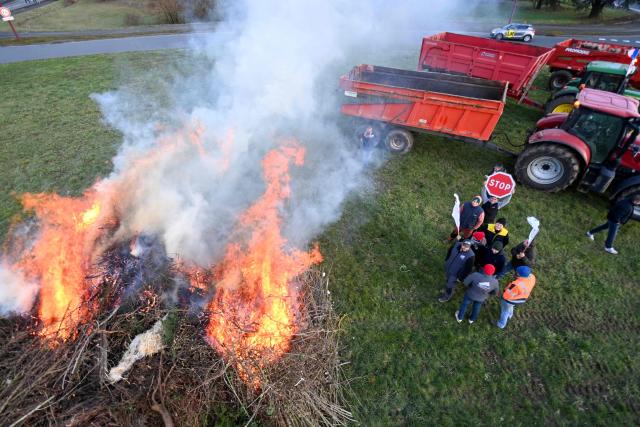 French farmers stand next to a fire they fed as they take part in a demonstration organized by French Farmers union FDSEA and JA Sarthe (Young Farmers Sarthe) to push French government to block the Mercosur trade deal and to protest against its handling of the nodular dermatitis (CND) epidemic  in front of the prefecture of Sarthe in Le Mans, Western France on January 9, 2026.  (Photo by JEAN-FRANCOIS MONIER / AFP)