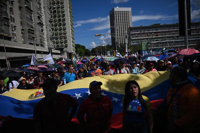 People hold a giant Venezuelan flag during a march in Caracas on January 9, 2026, to demand the release of deposed Venezuelan president Nicolas Maduro and his wife Cilia Flores, snatched and taken to New York on January 3 to face trial on drug and weapons charges. Colombia's President Gustavo Petro on January 9. urged Venezuela to jointly fight drug-traffickers operating across the two countries' border, after the United States threatened further armed action in the region. (Photo by Federico PARRA / AFP)