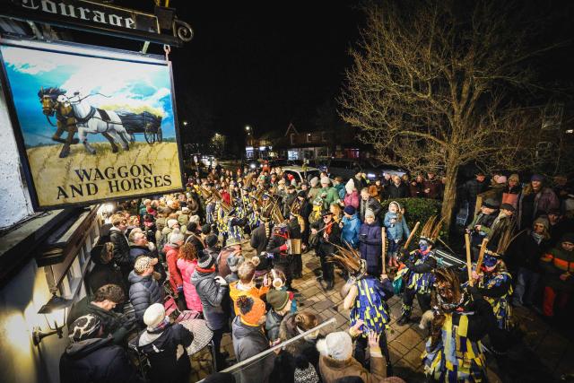 Villagers crowd across the pavement to watch as The Hook Eagle Morris Men dance outside The Waggon and Horses pub during the annual Wassail night in Hartley Wintney, west of London on January 9, 2026. The event, held near to Twelfth Night, celebrates both the passing of Christmas and the future good health of the fruit trees. Traditionally the custom involved the local farm workers visiting the orchard after dark with shotguns, horns, food and a large pail of cider. They would make a loud noise to raise the Sleeping Tree Spirit and to scare off demons. Cider would be poured over the roots and pieces of toast placed in the branches as a gift to the spirit of the tree. The wassail song is sung as a blessing or charm to bring fruitfulness or even in admonishment not to fail in the upcoming year. (Photo by Adrian DENNIS / AFP)