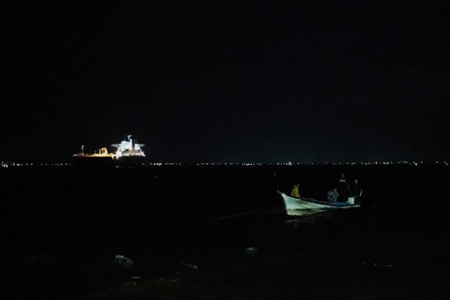 A boat sails while in the background is seen a crude oil tanker in the Maracaibo Lake in Maracaibo, Venezuela, on January 9, 2026. On January 8, three of 11 vessels chartered by Chevron were transporting oil from Venezuela to the US, according to an AFP analysis of ship-tracking data, as export sanctions raised concerns over the South American country's storage capacity. (Photo by Maryorin Mendez / AFP)