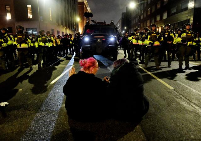 Two protesters sat on the road in front of Minnesota Conservation Officers as they were given the order to disperse after marching in protest against ICE for the fatal shooting of Renee Nicole Good in downtown Minneapolis, Minnesota on January 9, 2026. A US Immigration and Customs Enforcement (ICE) agent shot and killed 37-year-old Renee Nicole Good on the streets of Minneapolis on January 7, leading to huge protests and outrage from local leaders who rejected White House claims she was a domestic terrorist. (Photo by Octavio JONES / AFP)