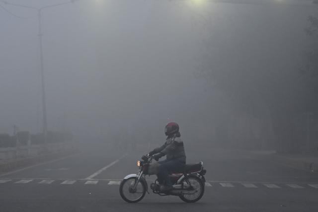 A man rides his bike amid dense fog on a cold winter morning in Lahore on January 10, 2026. (Photo by Arif ALI / AFP)