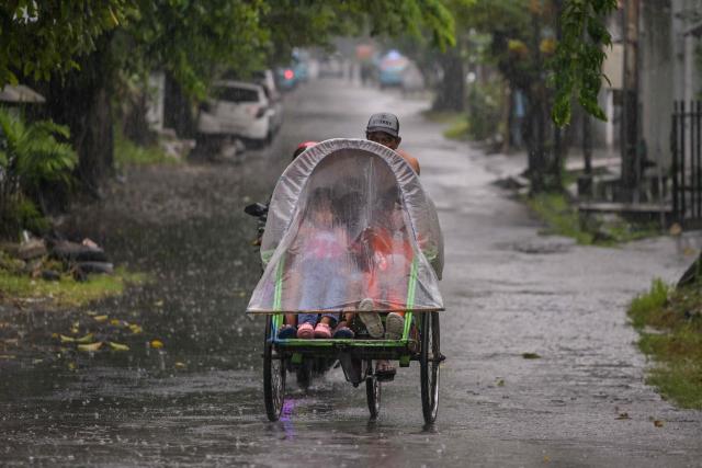 Children ride in a pedicab in the rain in Surabaya on January 10, 2026. (Photo by JUNI KRISWANTO / AFP)