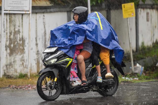 A man and his children ride a motorcycle in the rain in Surabaya on January 10, 2026. (Photo by JUNI KRISWANTO / AFP)