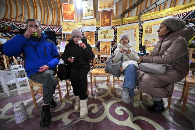 Members of the public drink free tea with traditional Kazakh bread baursaki, as they take the opportunity to get warm and charge their digital objects as part of the initiative "Yurt of Invincibility", organised by representatives of the Kazakh diaspora in a park in the center of Kyiv on January 10, 2026, amid Russian invasion in Ukraine. The Yurt of Invincibility is placed in a traditional Kazakh yurt and organised in a similar way with the Points of Invincibility, heating points organised by the government and volunteers around the country, as repeated Russian attacks have left Ukraine's energy grid teetering on the brink of collapse and have disrupted power and water supplies to millions over recent weeks. (Photo by Sergei SUPINSKY / AFP)