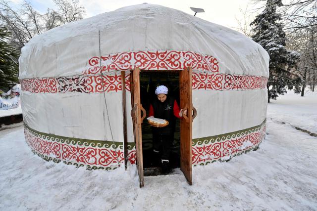 A volunteer leaves a yurt as she carries a traditional Kazakh bread baursaki, to cook it ouside as part of the "Yurt of Invincibility", organized by representatives of the Kazakh diaspora in a park in the center of Kyiv on January 10, 2026, amid Russian invasion in Ukraine. The Yurt of Invincibility is placed in a traditional Kazakh yurt and organized in a similar way with the Points of Invincibility, heating points organised by the government and volunteers around the country, as repeated Russian attacks have left Ukraine's energy grid teetering on the brink of collapse and have disrupted power and water supplies to millions over recent weeks. (Photo by Sergei SUPINSKY / AFP)