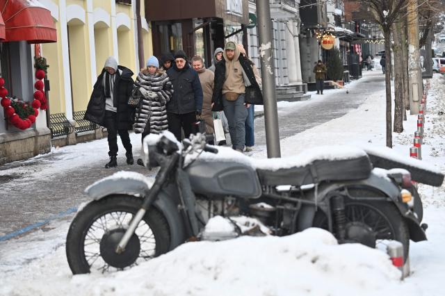 Passers-by walk past a snow-covered motorcycle in the center of Kyiv on January 10, 2026, amid Russian invasion in Uraine. (Photo by Sergei SUPINSKY / AFP)