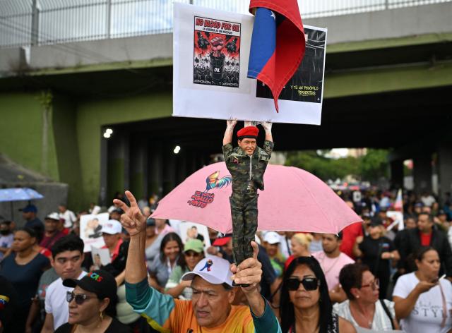 A man holds a figure of the late Venezuelan president (2002-2013) Hugo Chavez during a march in Caracas on January 10, 2026, to demand the release of deposed Venezuelan president Nicolas Maduro and his wife Cilia Flores, snatched and taken to New York on January 3 to face trial on drug and weapons charges. Venezuela was set to hold talks with US envoys in Caracas on restoring diplomatic ties, days after US forces deposed Nicolas Maduro as its president and US President Donald Trump's claimed to be "in charge" of the South American country. (Photo by Juan BARRETO / AFP)