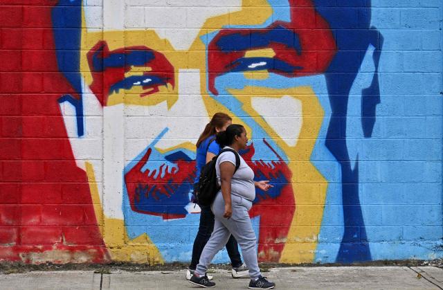 Women walk in front of a mural of ousted Venezuela's President Nicolas Maduro in Caracas on January 10, 2026. The US State Department on January 10, urged Americans in Venezuela to leave the country "immediately," citing risks from armed militias searching vehicles for US citizens at roadblocks. (Photo by Juan BARRETO / AFP)