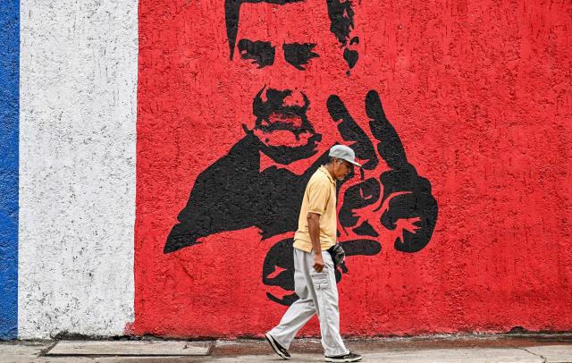 A man walks in front of a mural of ousted Venezuela's President Nicolas Maduro in Caracas on January 10, 2026. The US State Department on January 10, urged Americans in Venezuela to leave the country "immediately," citing risks from armed militias searching vehicles for US citizens at roadblocks. (Photo by Juan BARRETO / AFP)