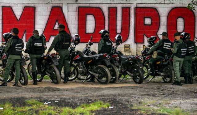 Members of the National Guard stand guard in front of a mural of ousted Venezuela's President Nicolas Maduro in Caracas on January 10, 2026. The US State Department on January 10, urged Americans in Venezuela to leave the country "immediately," citing risks from armed militias searching vehicles for US citizens at roadblocks. (Photo by Juan BARRETO / AFP)