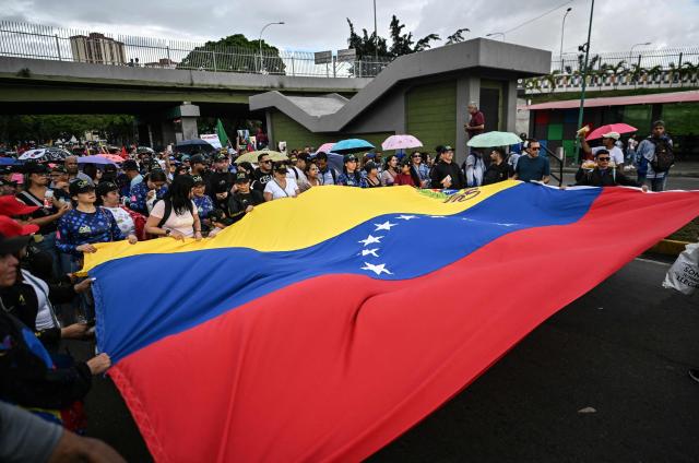 Demonstrators wave a giant Venezuelan flag during a rally in support of ousted Venezuela's President Nicolas Maduro in Caracas on January 10, 2026. The US State Department on January 10, urged Americans in Venezuela to leave the country "immediately," citing risks from armed militias searching vehicles for US citizens at roadblocks. (Photo by Juan BARRETO / AFP)