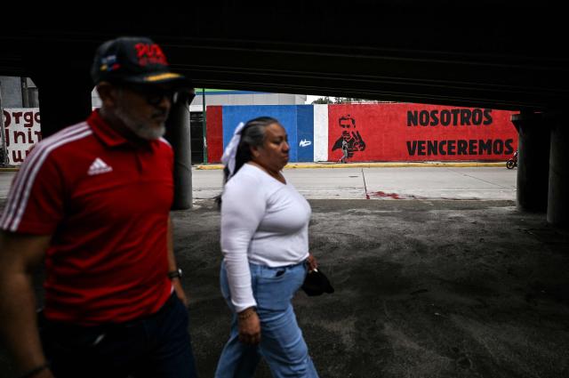 A couple walks in front of a mural of ousted Venezuela's President Nicolas Maduro in Caracas on January 10, 2026. The US State Department on January 10, urged Americans in Venezuela to leave the country "immediately," citing risks from armed militias searching vehicles for US citizens at roadblocks. (Photo by Juan BARRETO / AFP)