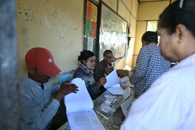 Election workers check voter registries for those arriving at a polling station during the second phase of Myanmar's general election at Kawhmu township in Yangon on January 11, 2026. Myanmar's junta opened polls on January 11 in the second phase of elections, continuing a vote democracy watchdogs say is letting the military prolong its rule in a civilian guise. (Photo by Sai Aung MAIN / AFP)