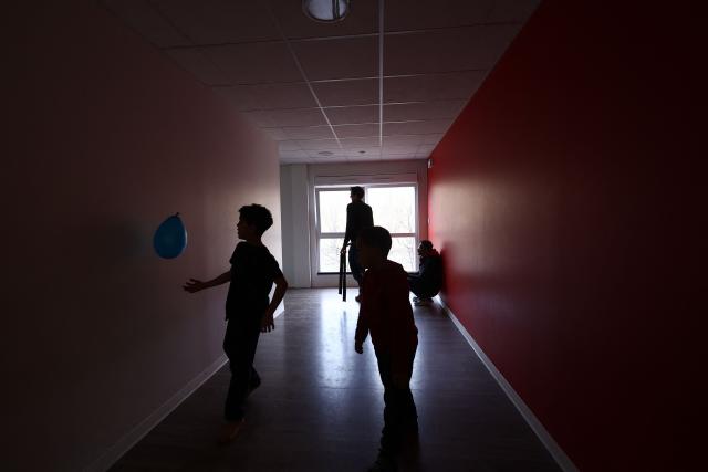 Two boys play in a corridor at an empty school near the Blandan's park in Lyon, south-eastern France, on January 10, 2026 where homeless families are being housed by a collective. Classrooms turned into dormitories and a cafeteria: more than 80 children without a roof over their heads are occupying an empty school in Lyon with their parents, in an operation of a "highly exceptional" scale carried out on January 9, 2026 evening by the collective "Jamais Sans Toit" (JST) due to the lack of housing solutions. (Photo by Alex MARTIN / AFP)