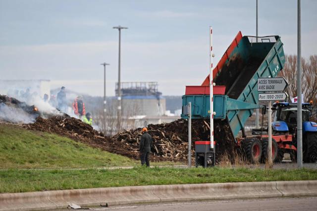A farmer truck pours piece of woods on a roundabout as part of national protests against the EU-Mercosur agreement and the government's handling of the contagious nodular dermatitis (CND) epidemic, on the port of Le Havre, northwestern France on January 11, 2026. Around a hundred farmers spent the night at the entrance to the port of Le Havre, western France to set up a "filtering roadblock" on January 11, 2026 and check trucks in order to denounce the agreement signed by the EU with the Mercosur countries, a spokesperson told AFP. (Photo by Lou BENOIST / AFP)