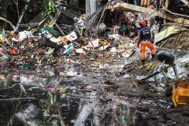 Members of the search and rescue team look for people after a landslide at the landfill in Barangay Binaliw, Cebu City on January 11, 2026. Hard hat-wearing rescue workers and backhoes dug through rubble in search of survivors on January 10 in the shadow of a mountain of garbage that buried dozens of landfill employees in the central Philippines, killing at least six. (Photo by Cheryl Baldicantos / AFP)