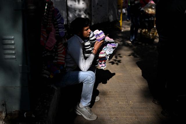 A vendor selling socks uses his cell phone as he waits for customers at a marketplace in New Delhi on January 11, 2026. (Photo by Sajjad HUSSAIN / AFP)