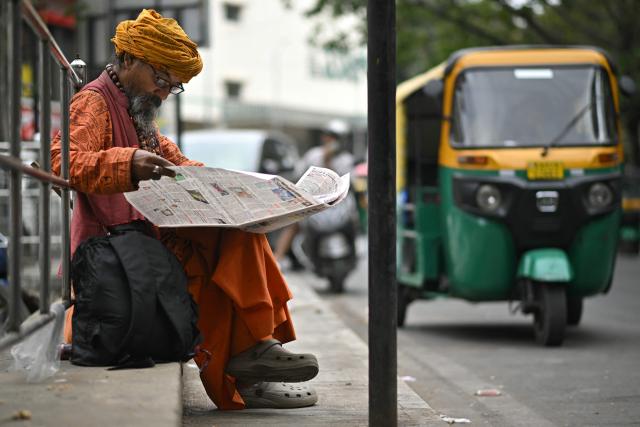 A Hindu holy man reads a newspaper along a pavement in Bengaluru on January 11, 2026. (Photo by Idrees MOHAMMED / AFP)