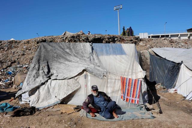 TOPSHOT - A displaced Palestinian man warms-up in the sun as he sits outside a family tent shelter set-up in Gaza City on January 11, 2026. The majority of Gaza's 2.4 million people have been displaced, often multiple times, by the war that began with Hamas's attack on southern Israel on October 7, 2023. With displaced families living in tented camps, a serious concerns has been raised over their living conditions. (Photo by Omar AL-QATTAA / AFP)