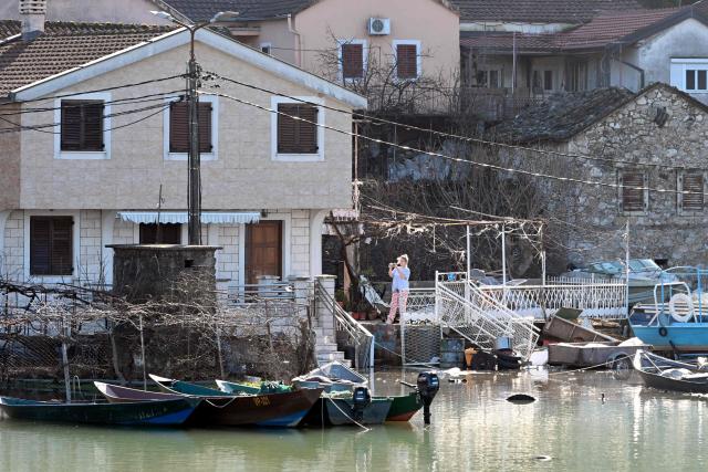 A resident takes pictures in front of flooded houses in the fishermen's village of Vranjina, on the shores of Skadar lake, 25km South of Montenegro's capital of Podgorica, on January 11, 2026. Water level at Skadar lake has risen after heavy rain hit the area, causing a massive overflow on artificial lakes in neighboring Albania. (Photo by SAVO PRELEVIC / AFP)