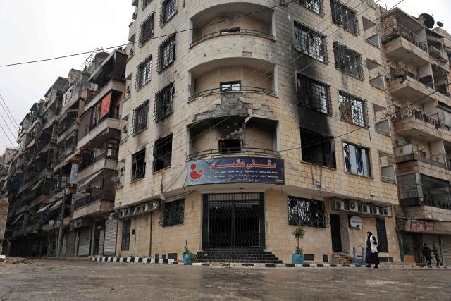 A woman walks past a damaged building following a ceasefire in the Kurdish-majority Ashrafiyeh neighbourhood of the city of Aleppo, northern Syria on January 11, 2026. Syria's Kurdish fighters said on January 11, 2026, that they agreed under a ceasefire to withdraw after days of fighting government forces in the city. The latest clashes erupted after negotiations to integrate the Kurds into the country's new government stalled. (Photo by OMAR HAJ KADOUR / AFP)
