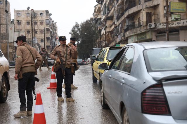 Syrian security officers stand at a checkpoint controlling passing vehicles following a ceasefire in the Kurdish-majority Ashrafiyeh neighbourhood of the city of Aleppo, northern Syria on January 11, 2026. Syria's Kurdish fighters said on January 11, 2026, that they agreed under a ceasefire to withdraw after days of fighting government forces in the city. The latest clashes erupted after negotiations to integrate the Kurds into the country's new government stalled. (Photo by OMAR HAJ KADOUR / AFP)