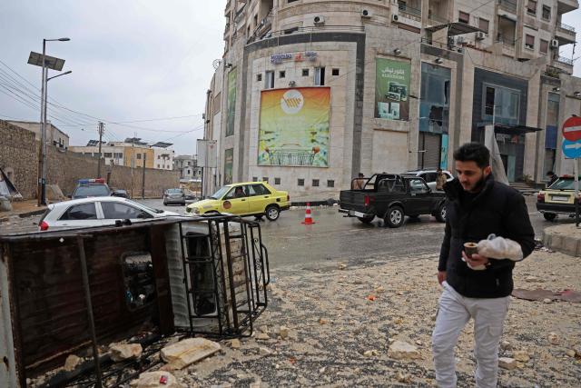 A man walks past an overturned van and its contents, following a ceasefire in the Kurdish-majority Ashrafiyeh neighbourhood of the city of Aleppo, northern Syria on January 11, 2026. Syria's Kurdish fighters said on January 11, 2026, that they agreed under a ceasefire to withdraw after days of fighting government forces in the city. The latest clashes erupted after negotiations to integrate the Kurds into the country's new government stalled. (Photo by OMAR HAJ KADOUR / AFP)