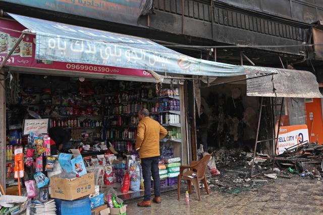 A man stands at the entrance of an open shop located next to a destroyed shop, following a ceasefire in the Kurdish-majority Ashrafiyeh neighbourhood of the city of Aleppo, northern Syria on January 11, 2026. Syria's Kurdish fighters said on January 11, 2026, that they agreed under a ceasefire to withdraw after days of fighting government forces in the city. The latest clashes erupted after negotiations to integrate the Kurds into the country's new government stalled. (Photo by OMAR HAJ KADOUR / AFP)