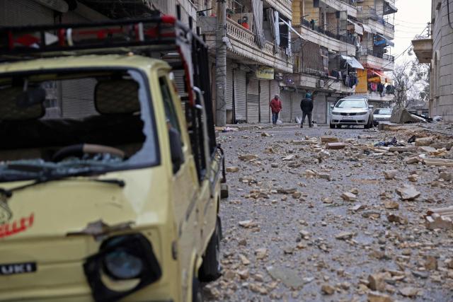 People walk past rubble and masonry from a a damaged building strewn across a street, following a ceasefire in the Kurdish-majority Ashrafiyeh neighbourhood of the city of Aleppo, northern Syria on January 11, 2026. Syria's Kurdish fighters said on January 11, 2026, that they agreed under a ceasefire to withdraw after days of fighting government forces in the city. The latest clashes erupted after negotiations to integrate the Kurds into the country's new government stalled. (Photo by OMAR HAJ KADOUR / AFP)
